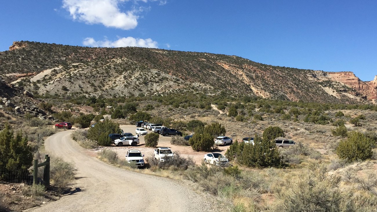 gravel road leads to dirt parking lot, backdrop of sparsely vegetated canyon slops