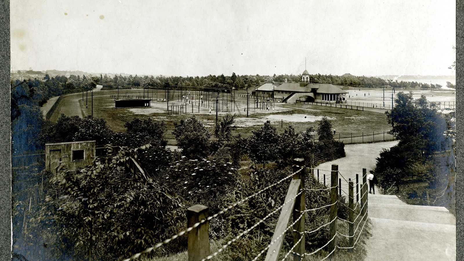 Black and white of playground area with lots of metal ladders, grass around edges, trees after