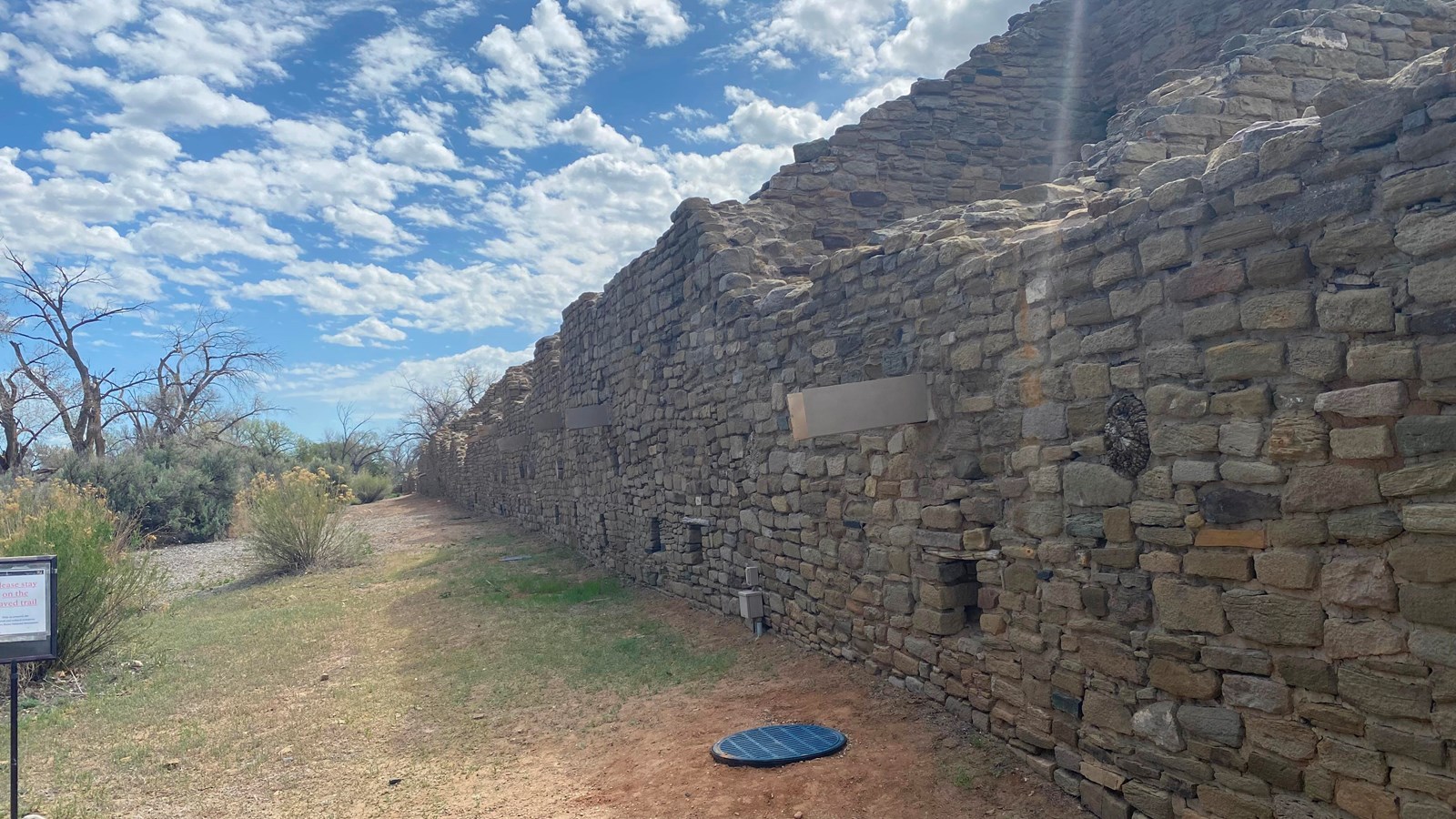 A long, straight sandstone wall facing east to west under a blue sky.