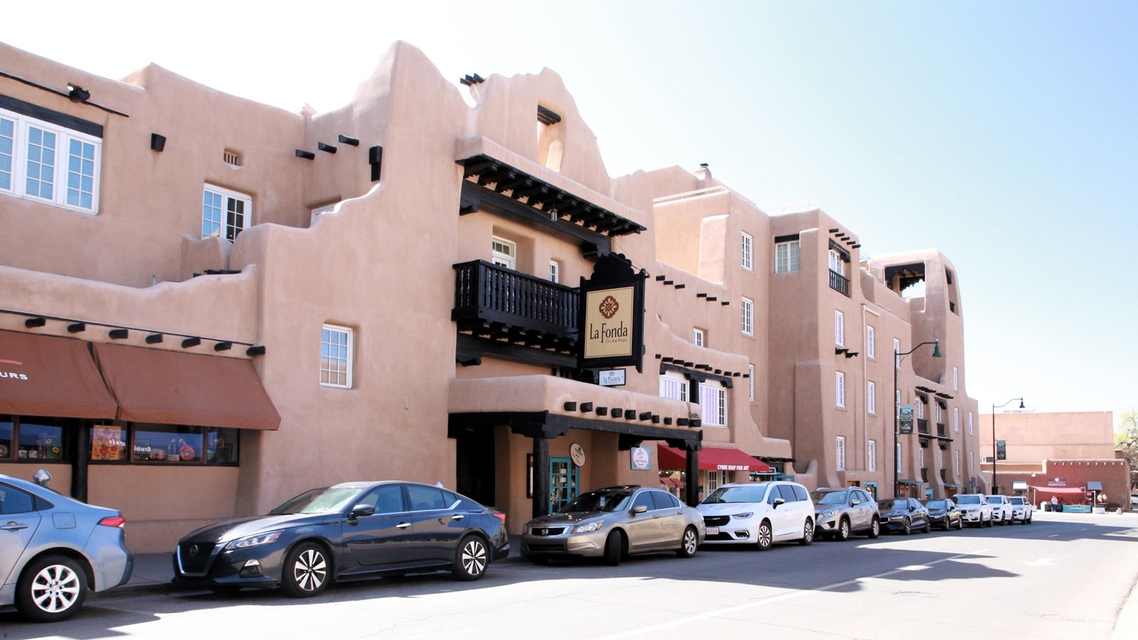 A large, two-story, pink adobe building, on a city street lined with cars.