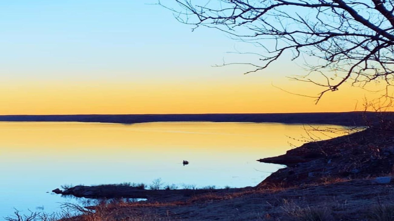 A yellow and turquoise sunset at North Point View.  The lake is calm with one boat floating. 