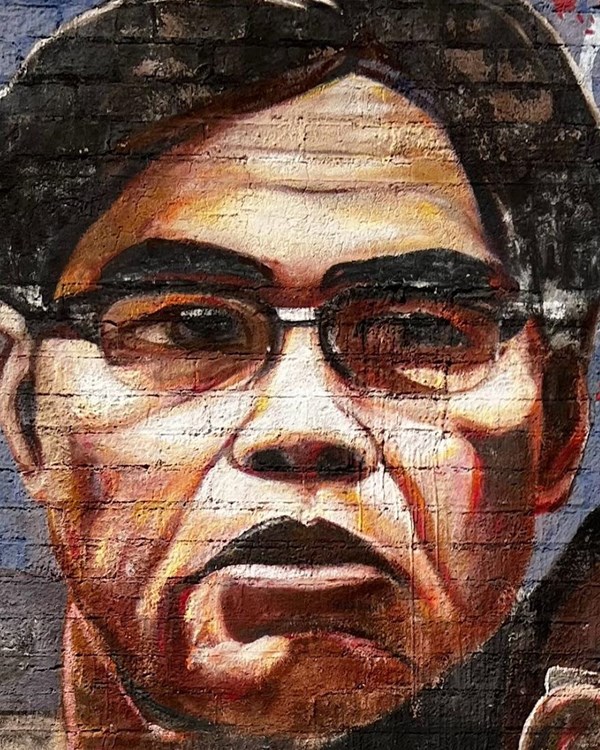 Mural painting of Philip Vera Cruz, a person with black hair, brown skin, glasses.