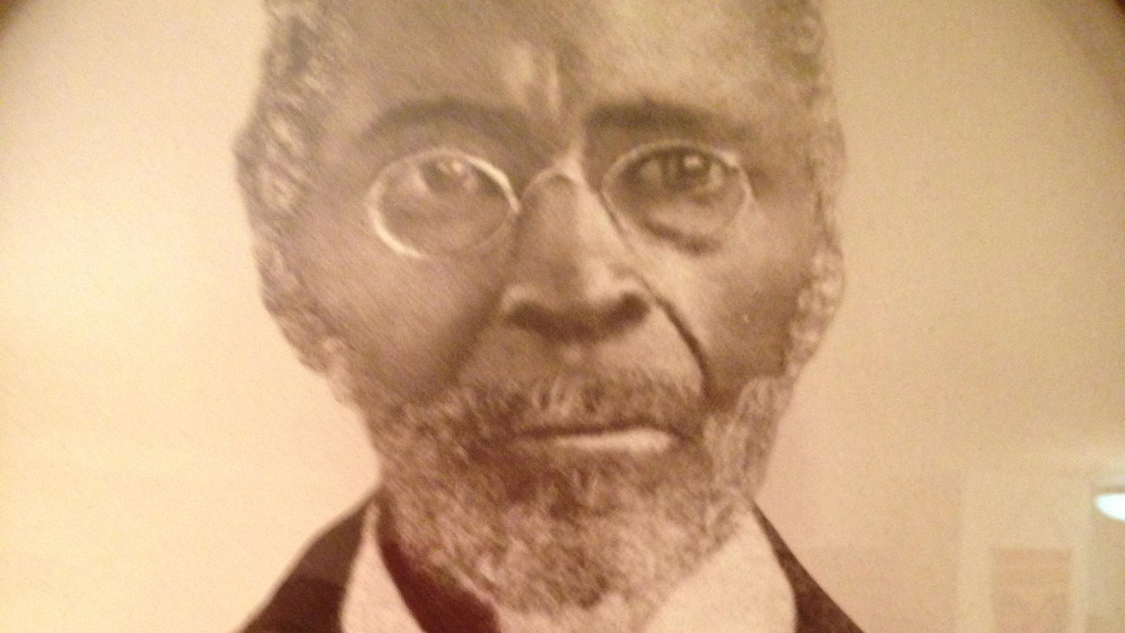 An African American man with glasses and a full beard. He is wearing a suit with a bow tie.