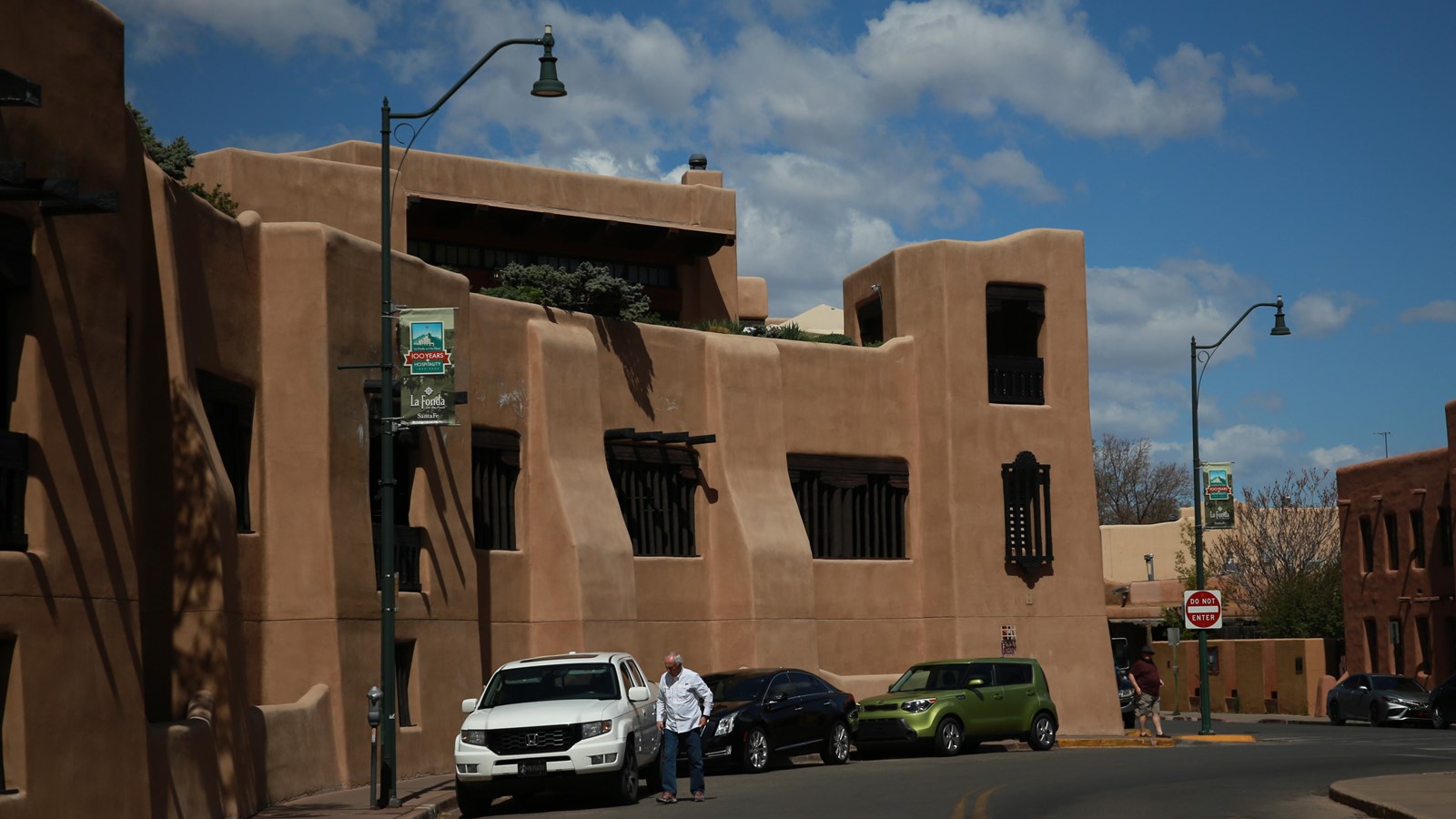 Cars parked on a street next to a peach stucco, three story parking garage.