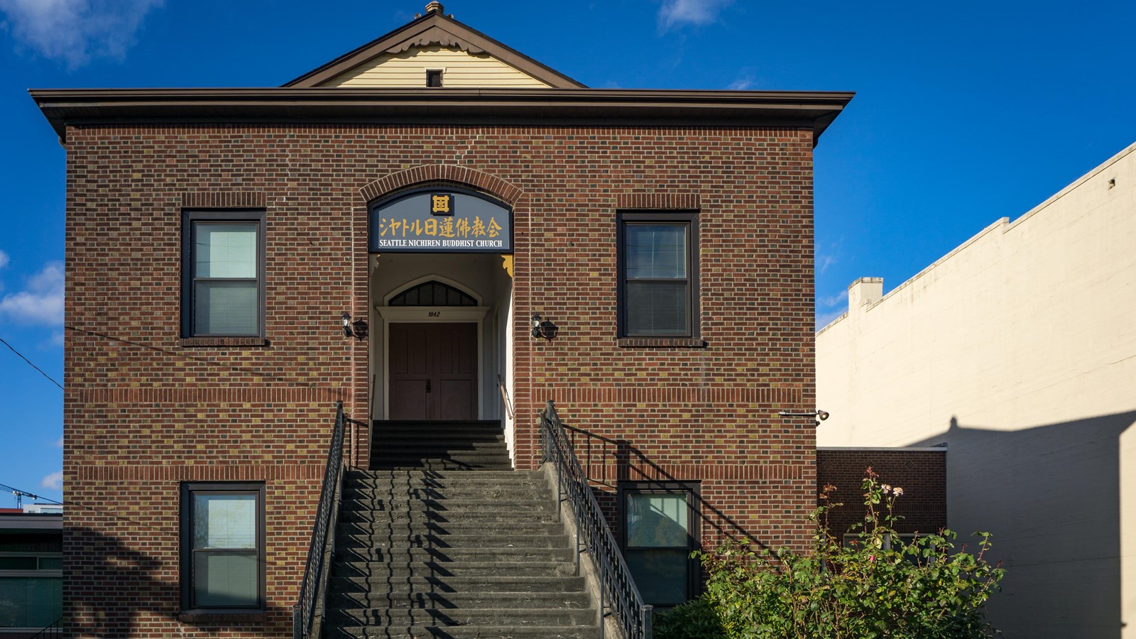 A brick building with a staircase leading up to its entrance. The scene is well-lit by a blue sky.