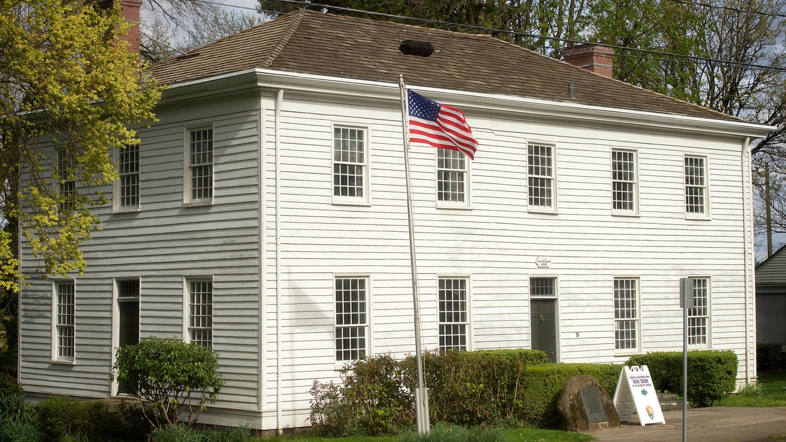 A white square house with an American flag on a flagpole outside.