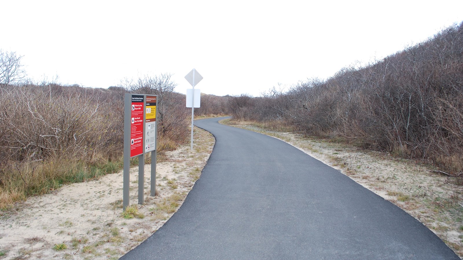 Entrance to the paved bike trail with regulation signage and bushes.