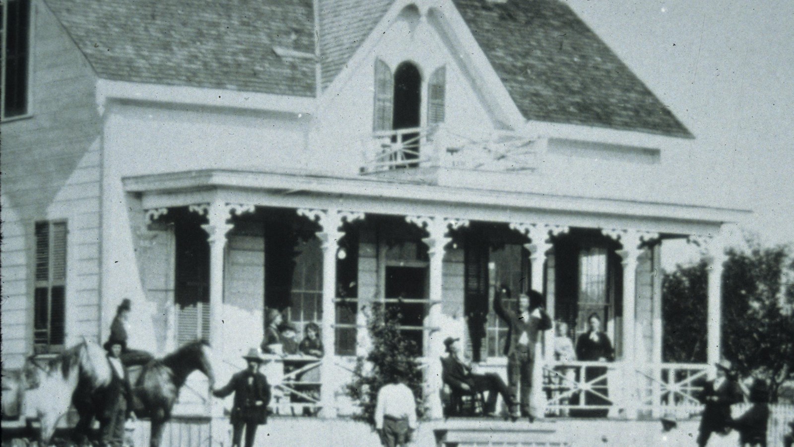 Black and white photo of group on porch of white two story Victorian house.