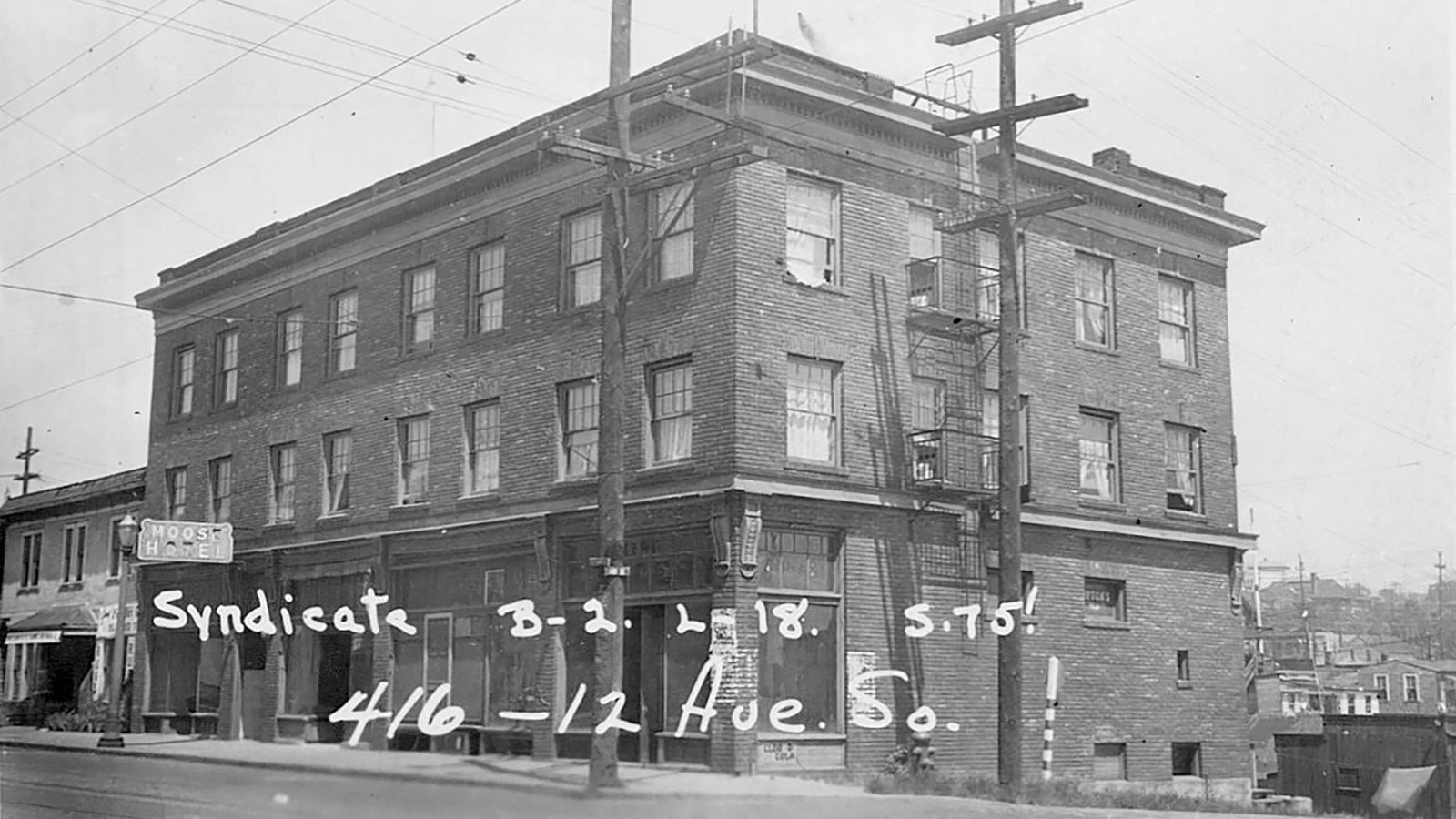 The building is made of brick and has three stories. Visible are utility poles and a fire escape.