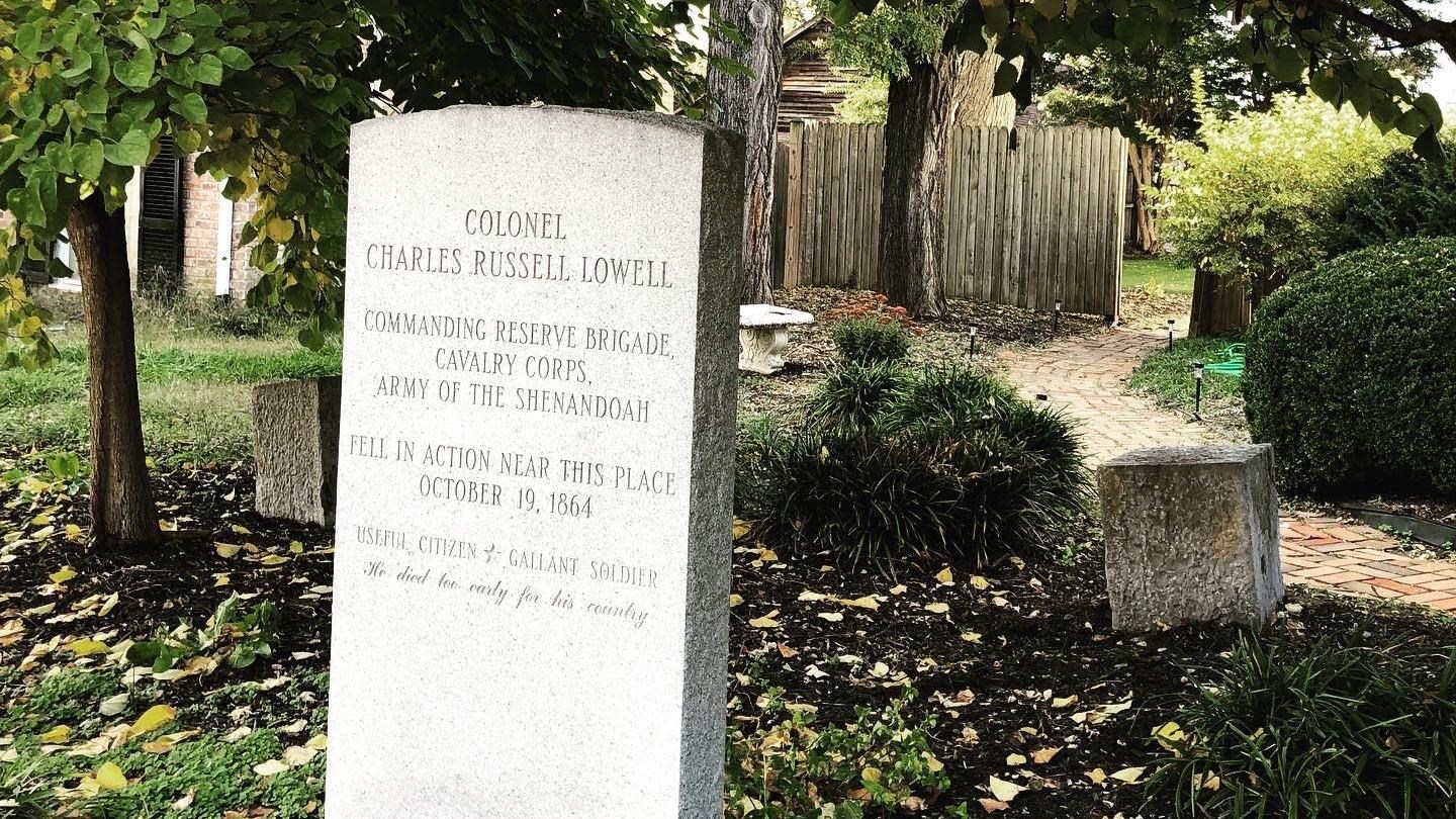 A stone marker on a shady town street commemorates a fallen soldier.