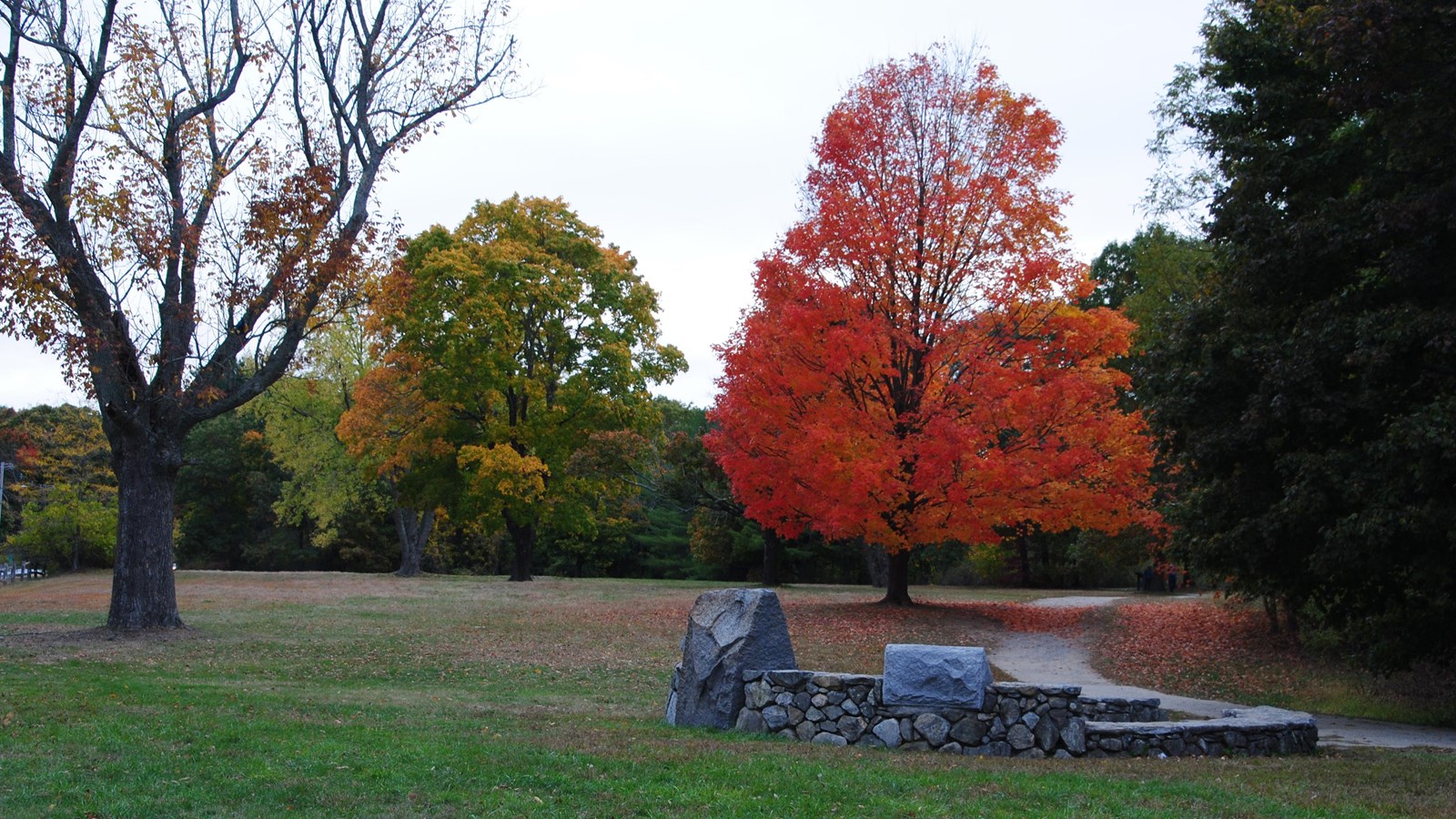 Stone monument and circle set within a field and trail with a few trees in autumn color.