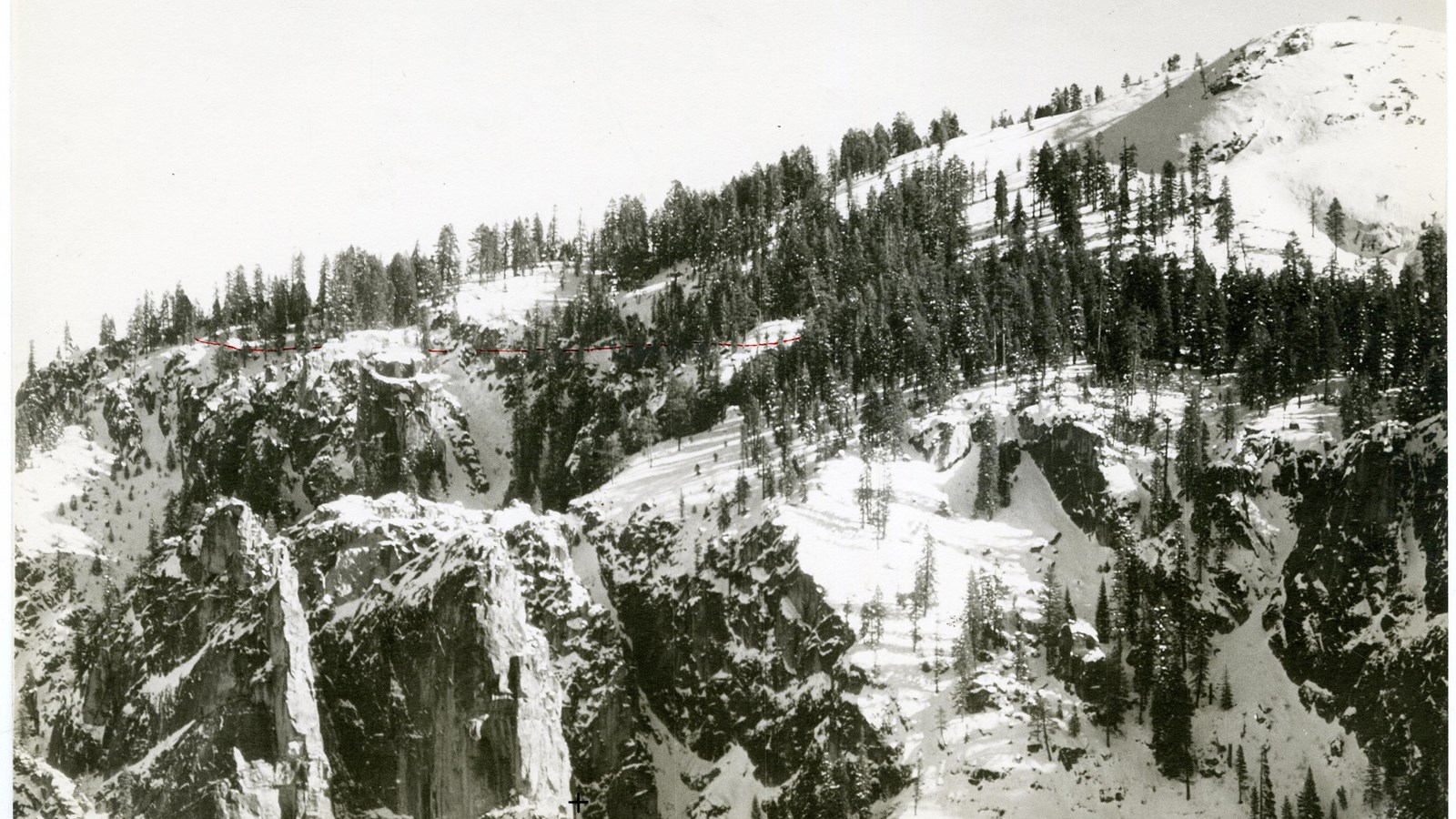 Black and white of rocky mountain top covered with snow and trees spread out on top