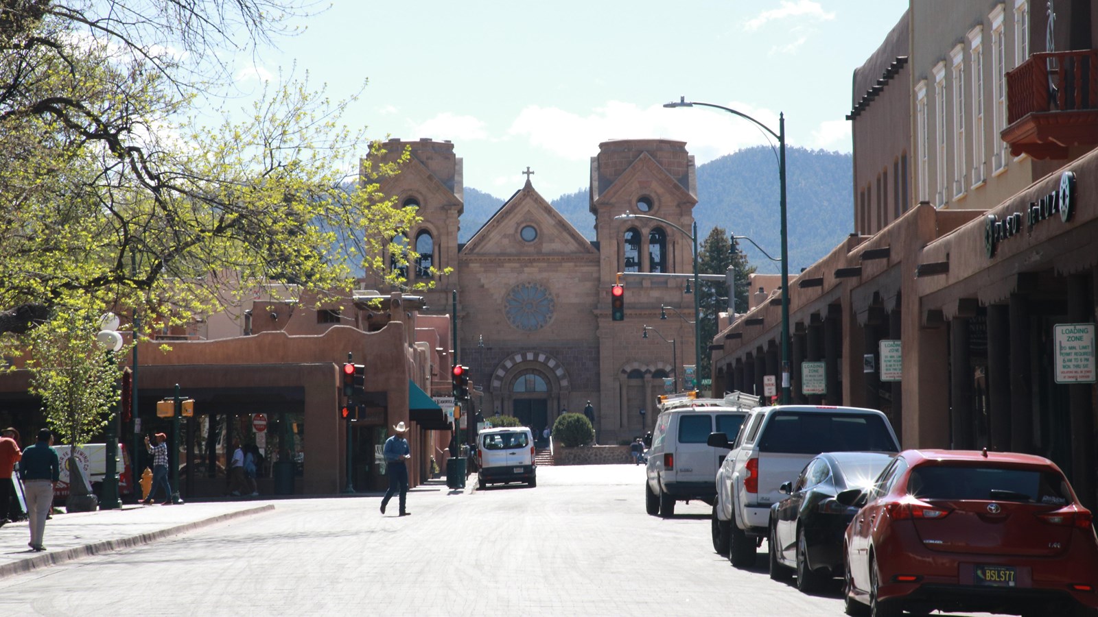 Looking down a city street lined with cars and one and two story adobe historic buidlings.