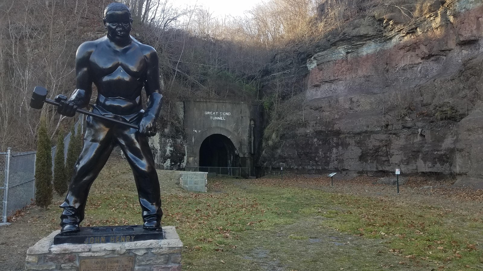 A statue of John Henry stands in front of a railroad tunnel 