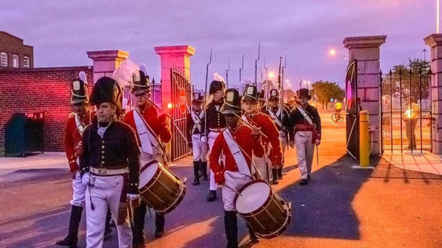 The Fort McHenry Guard is marching through the open Main Gate. They are led by an NCO and drummers.