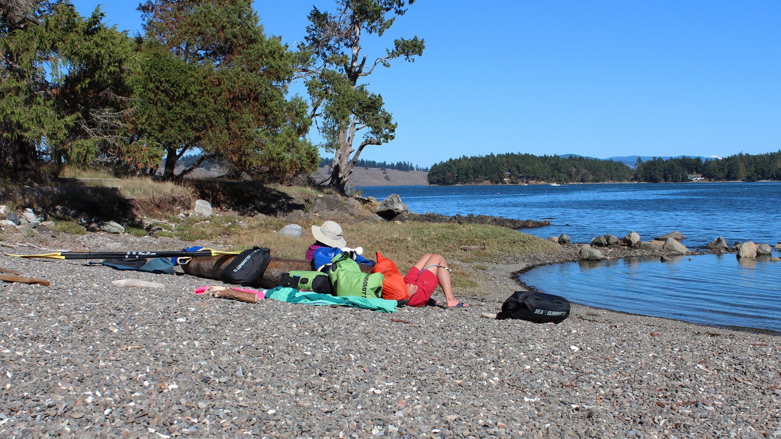 a man snoozes on a rocky beach with a kayak nearby