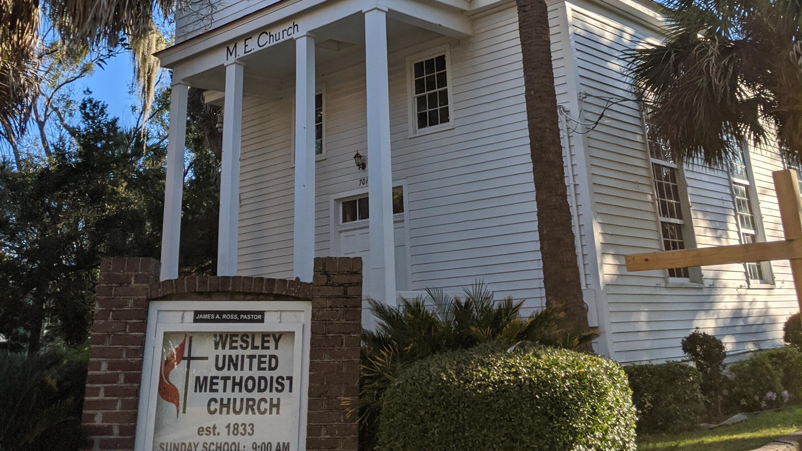 A small white wooden chapel with a brick sign noting the name of the church