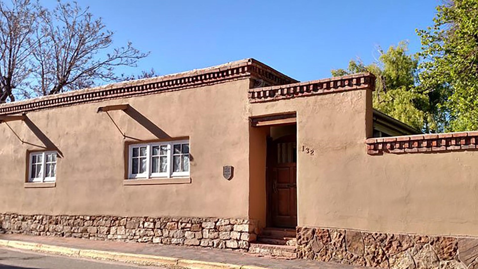 A one, story modest adobe home with brick design along the flat roof.