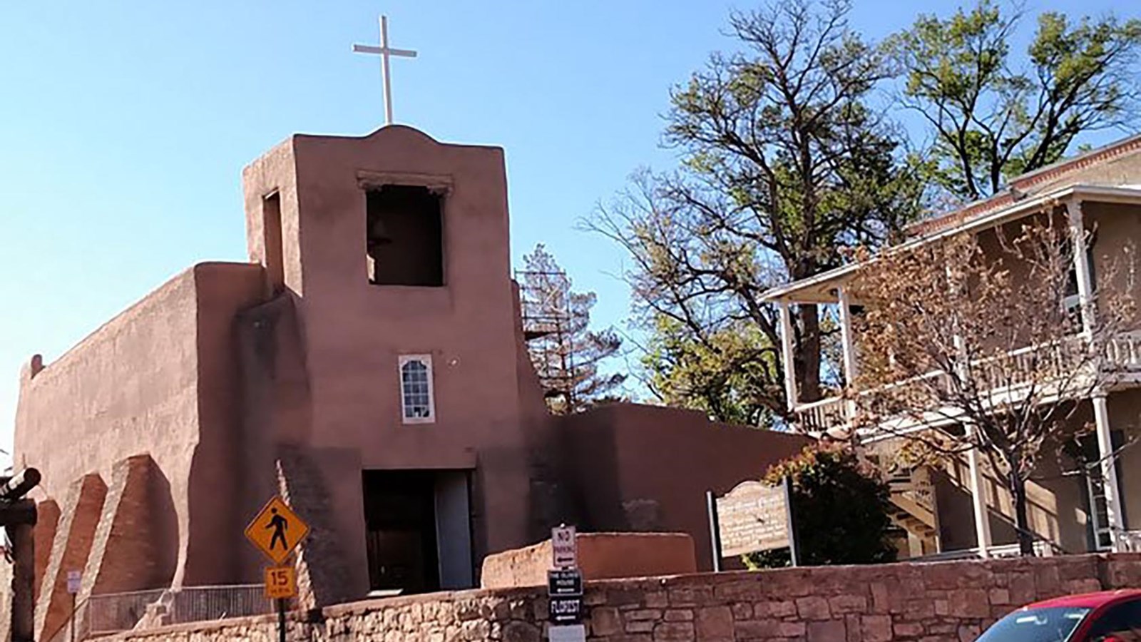 A small adobe, single tower chapel with a stone wall surrounding it.