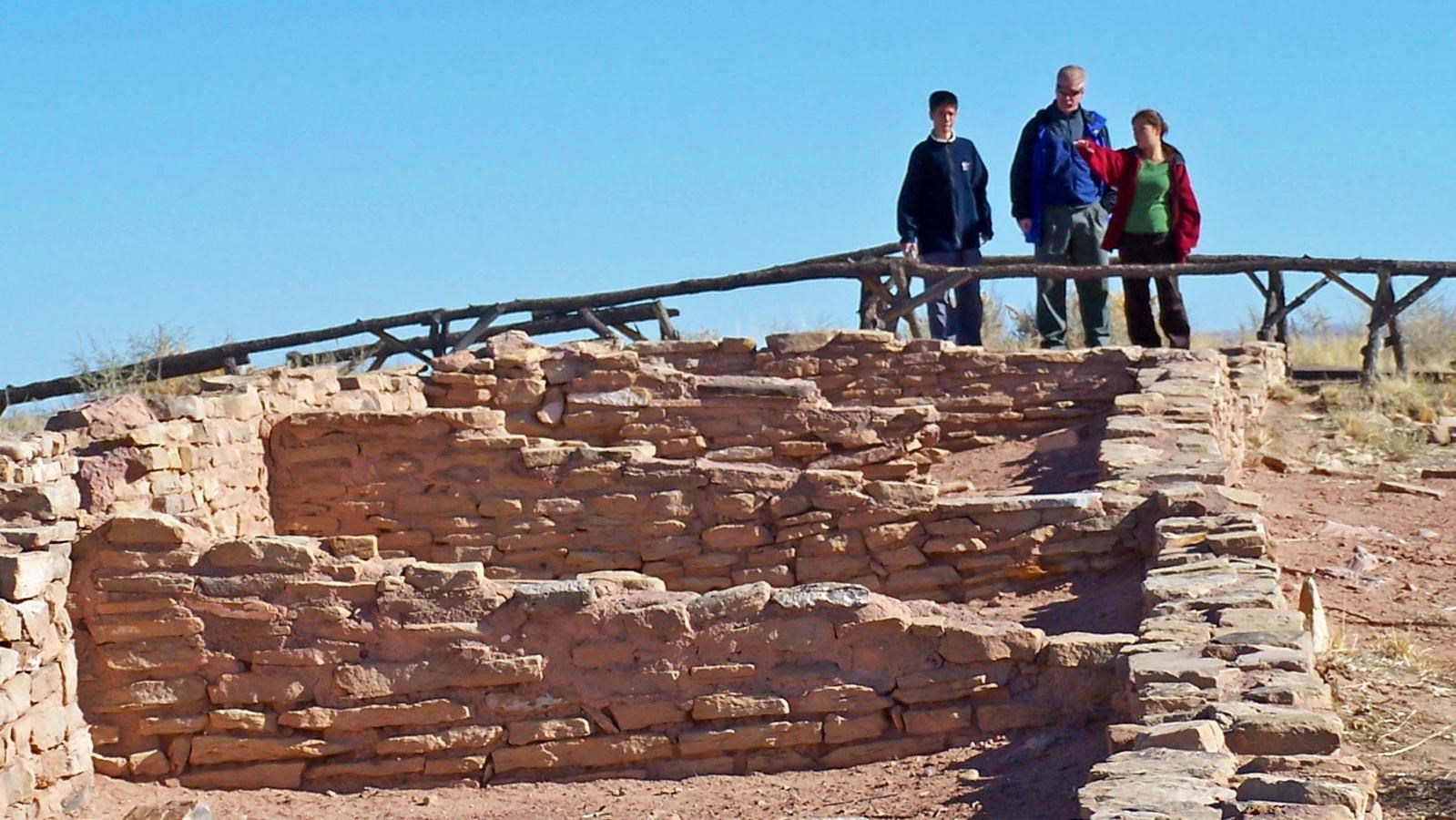 Family looking at masonry walls of an archeological site under a blue sky.