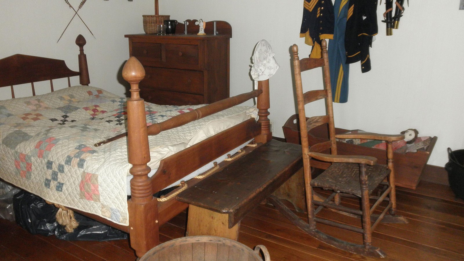 Bed with quilt and posts with clothing hanging on wall pegs