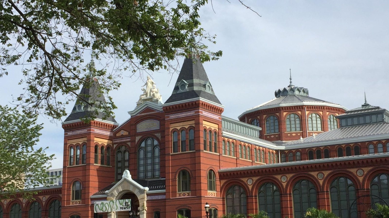Front entrance of a red brick building with two pointed towers and a central metal rotunda.