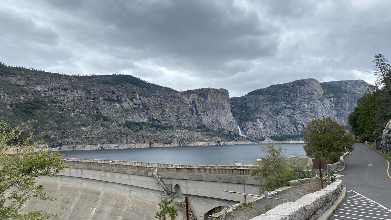 A concrete dam in front of a large body of water and granite cliffs above