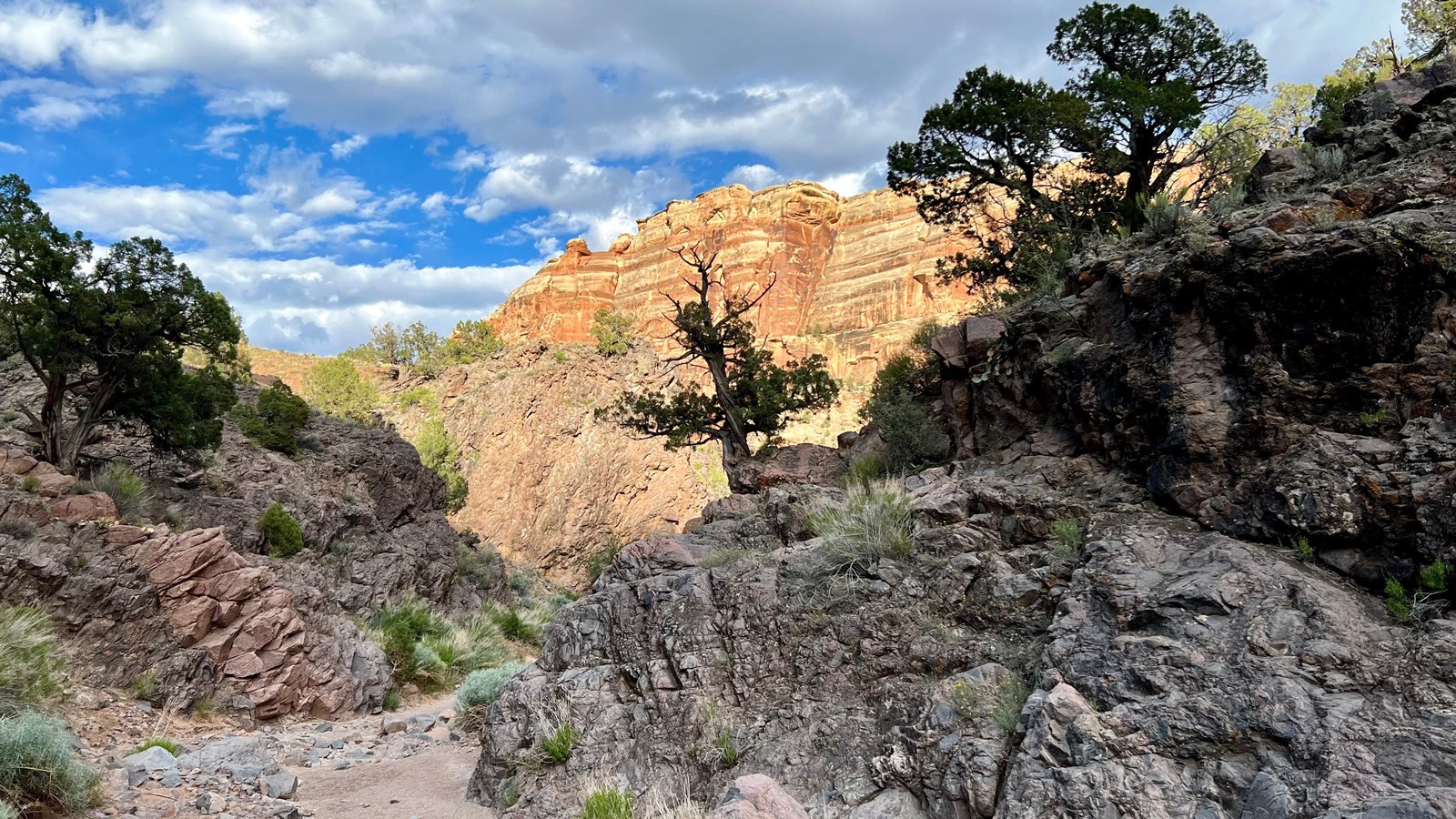 red-orange sandstone cliffs illuminate in sunset above dark gray, craggy canyon bottoms