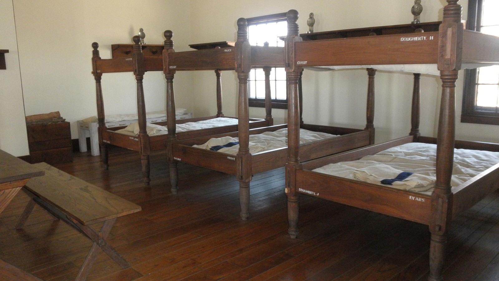 three wooden bunk beds lined up in a rowl. Each bunk bed has a name.Bunk beds are in a large room.