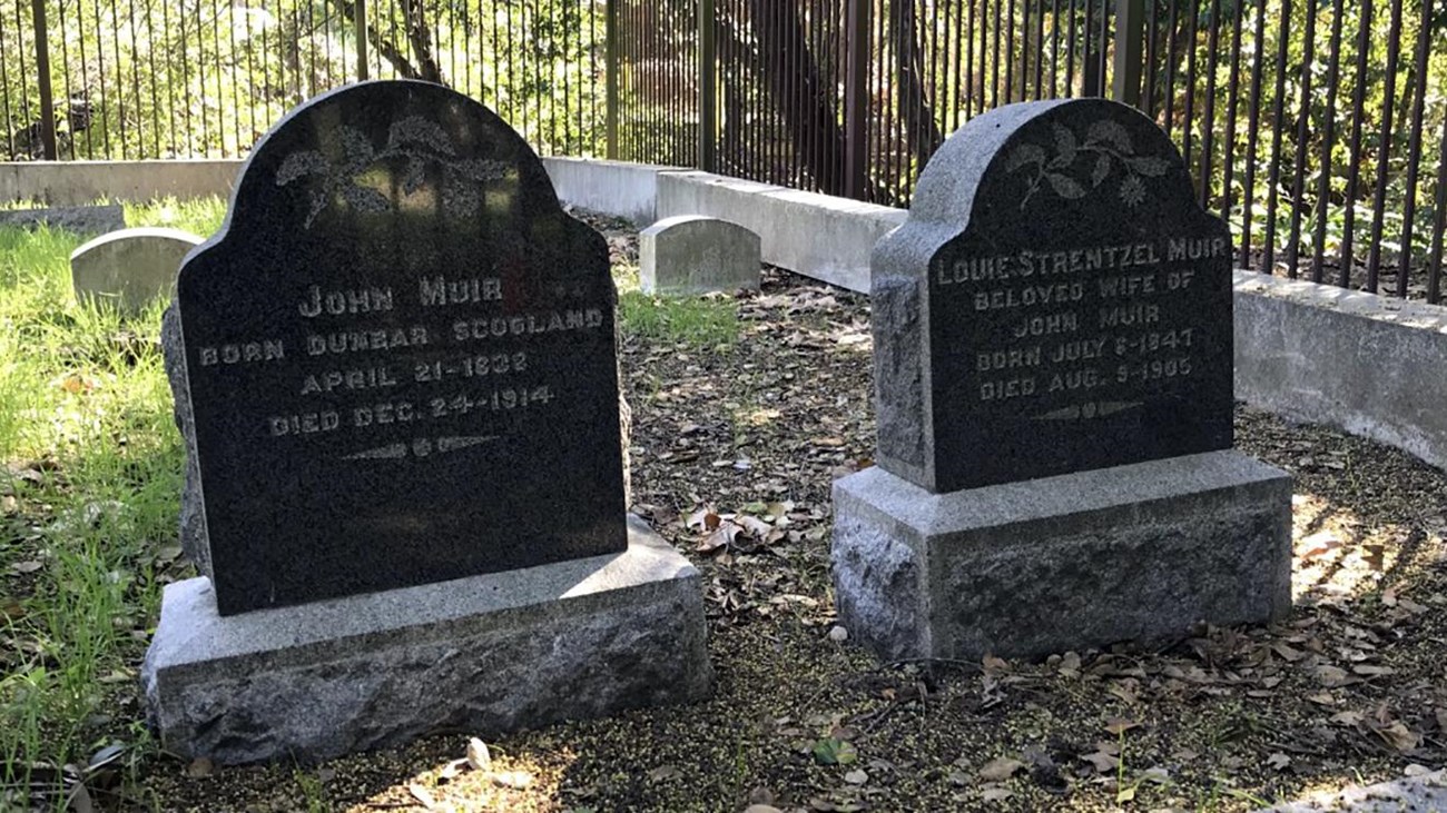 Two gravestones set amongst some grass and trees. 