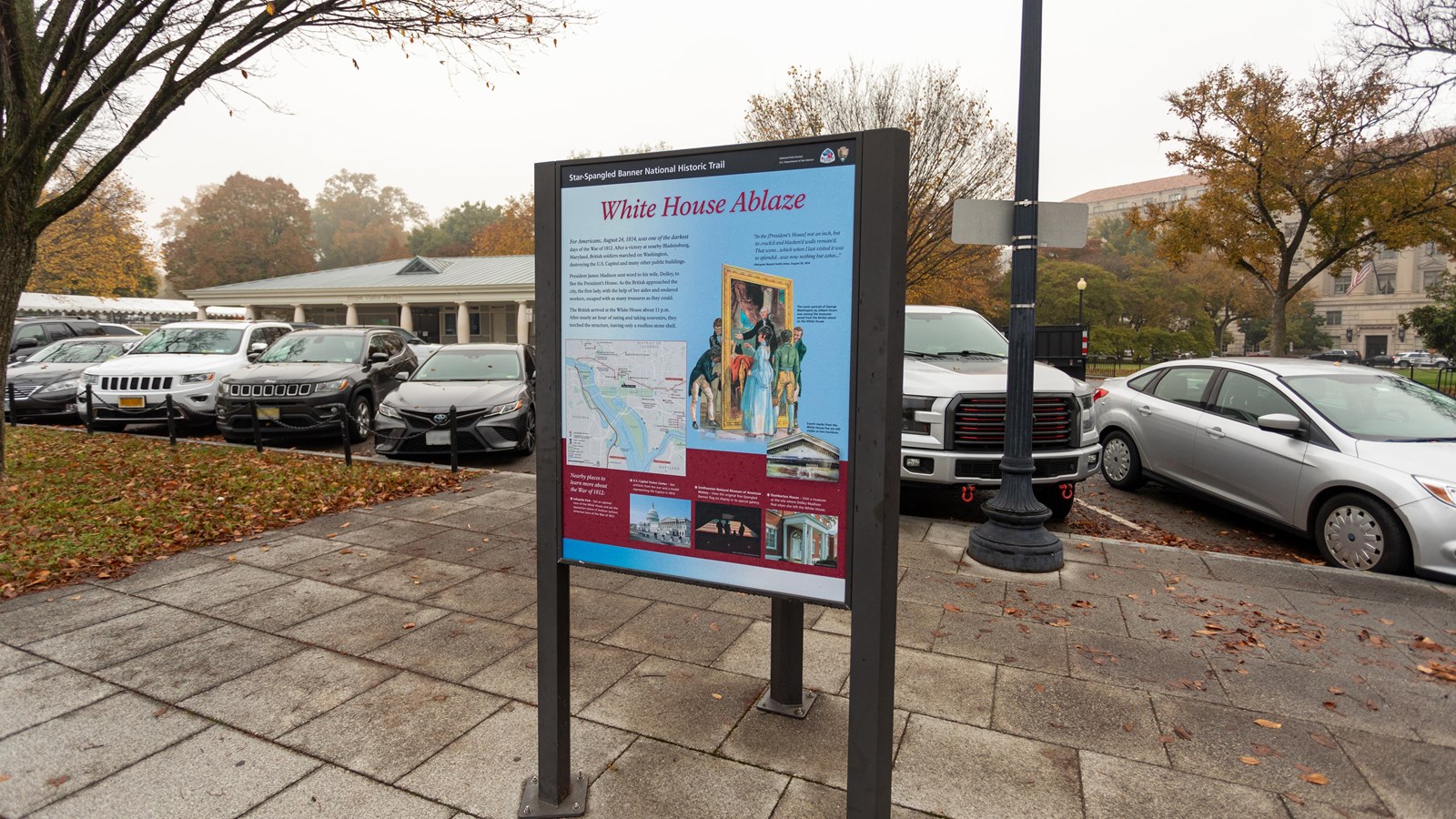 Interpretive panel on walkway near parked cars.