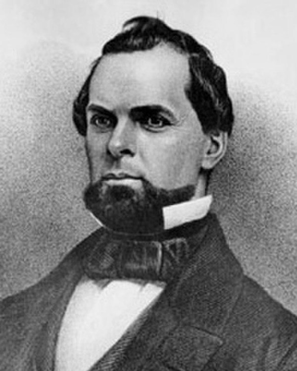 A man with a black jacket, white shirt and black tie.