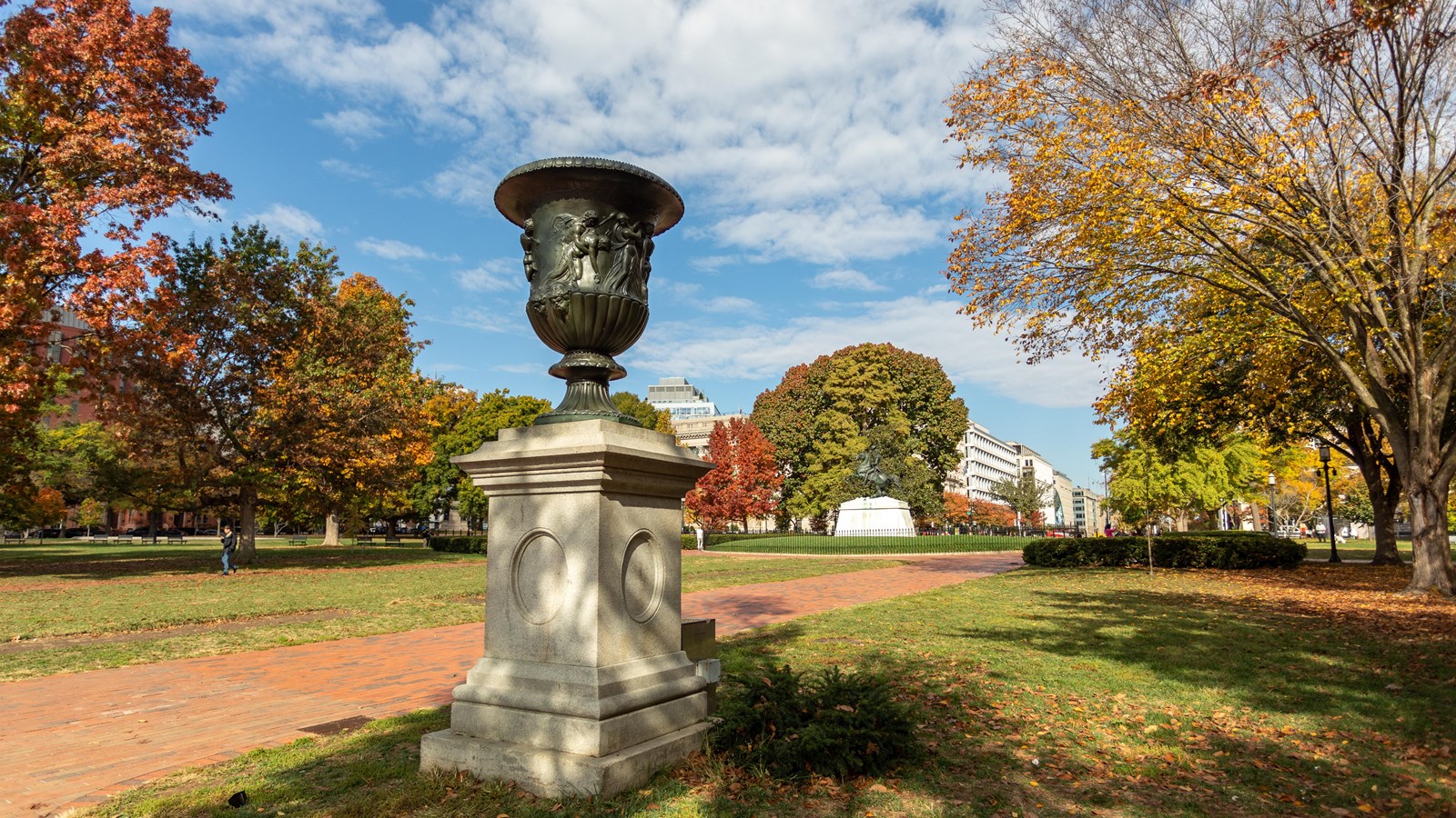 A bronze urn with depictions of people on it on a pedestal in front of the White House.
