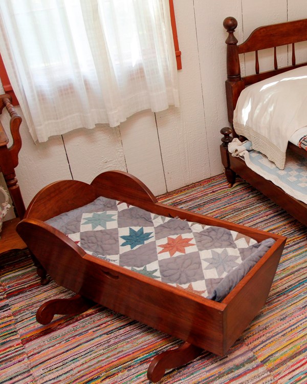Wooden bed and wooden cradle in a room side by side. Multicolor blankets cover both items.