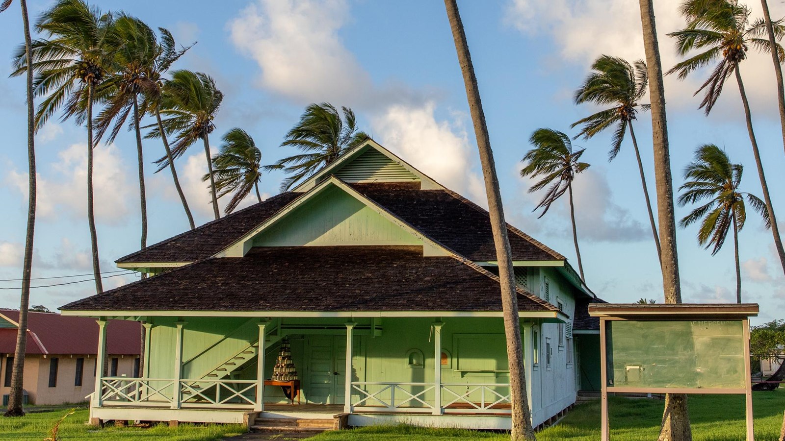 A green building with a darker roof surrounded by palm trees.