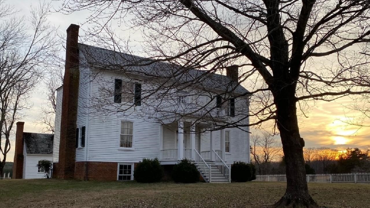 A white two-story wooden frame house with the sunset in the background.