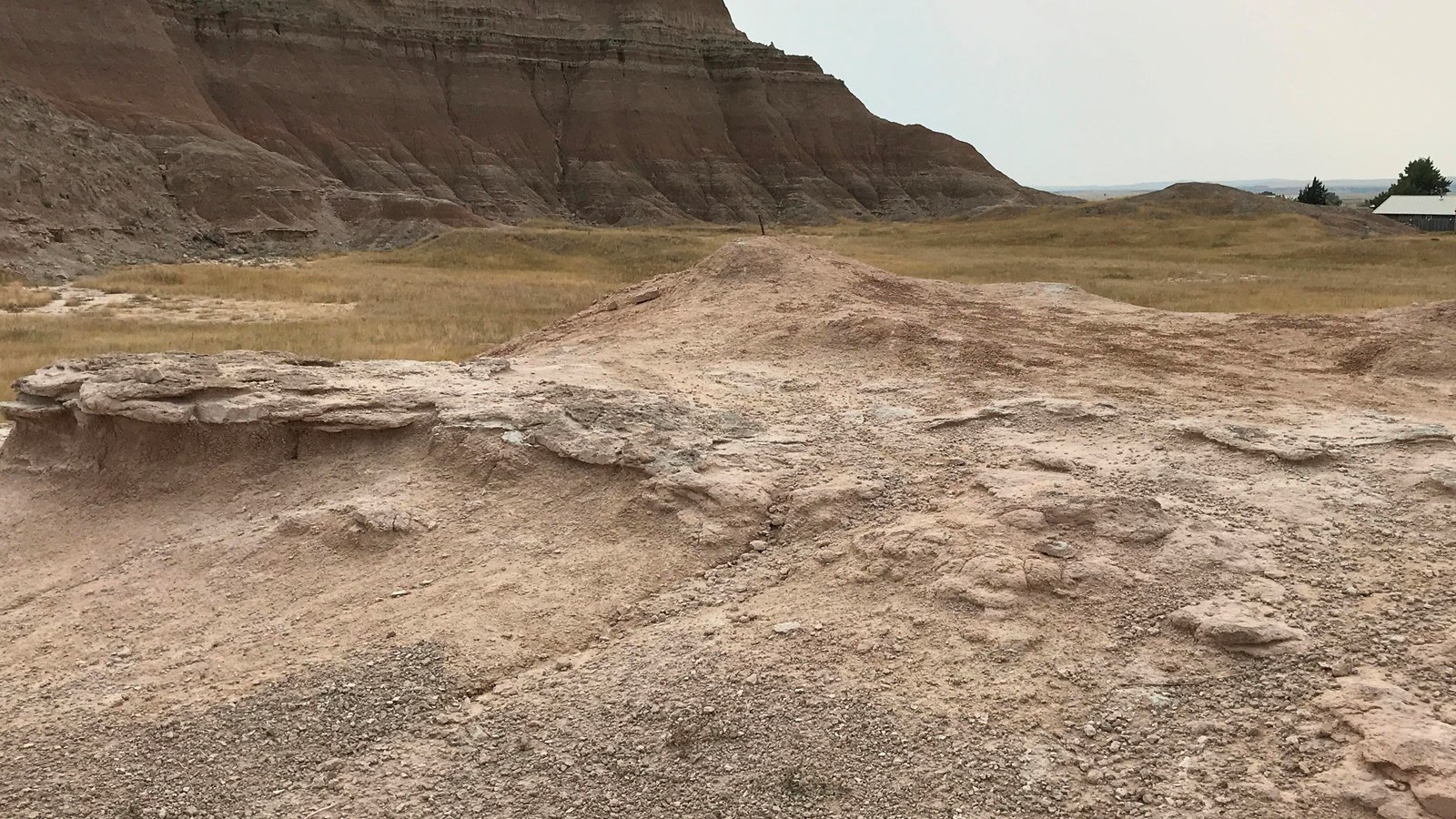 A heap of dirt with badlands buttes in background below blue sky.
