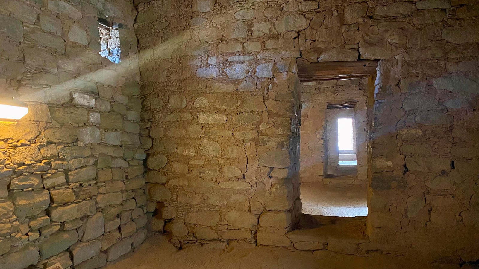 The interior of a room with tall sandstone walls & a series of open doorways in a row to other rooms