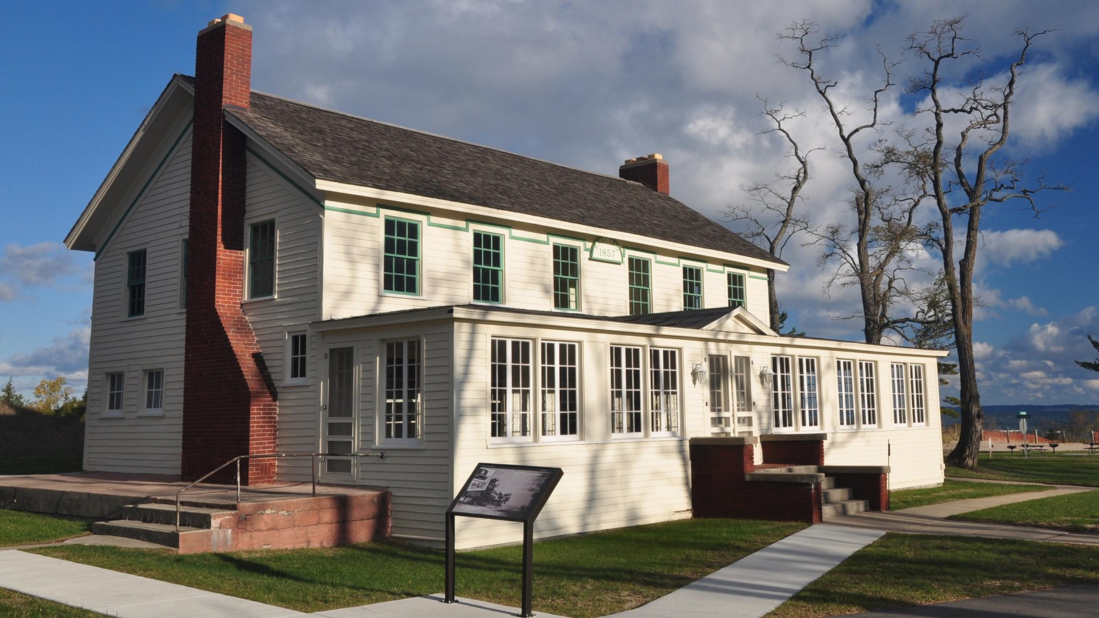 Sun brightens the front of a white, two-storied building with an enclosed front porch.