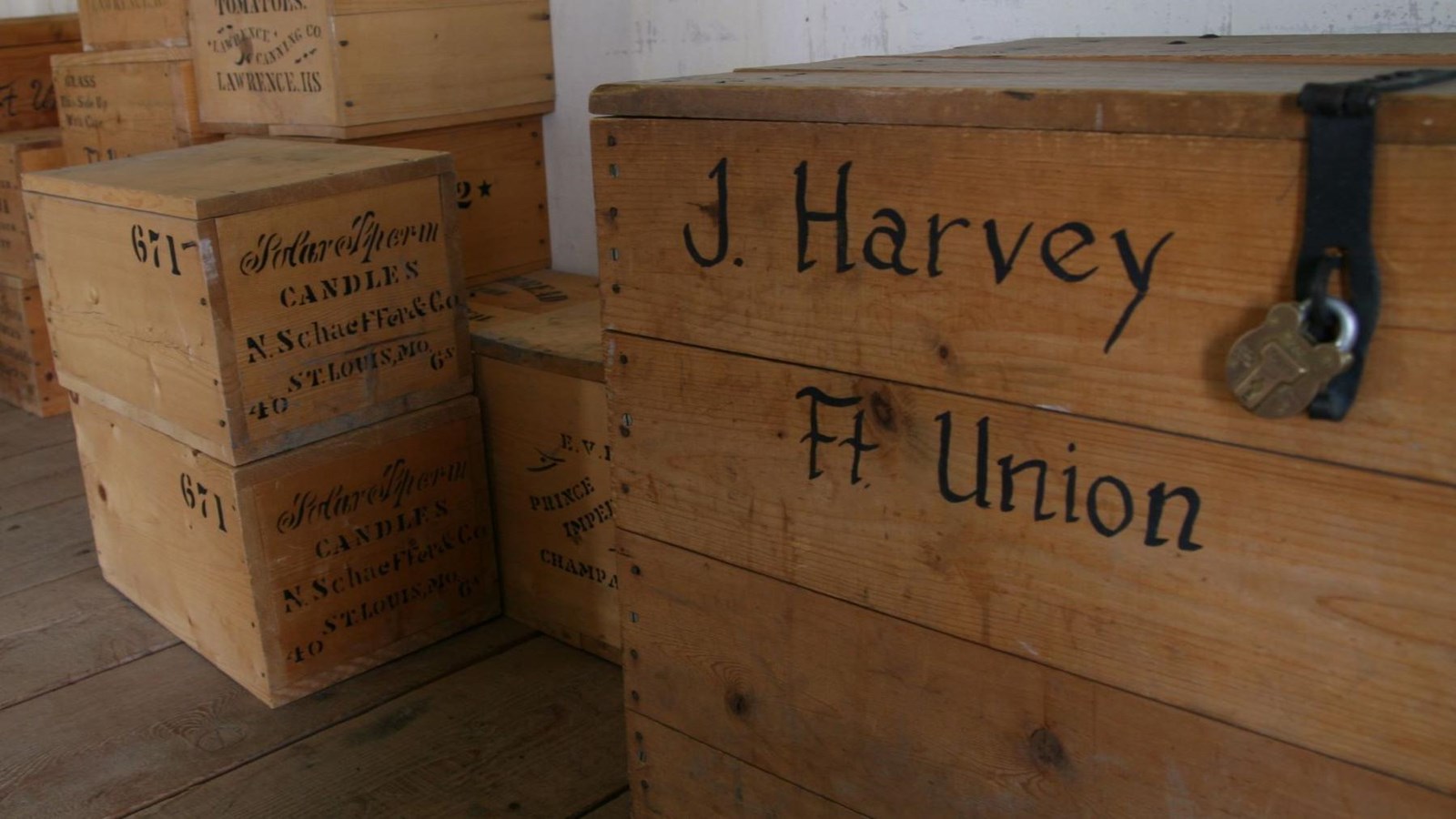 Wooden crates stacked against white wall, written: Candles, tomatoes, J. Harvey, Ft. Union.