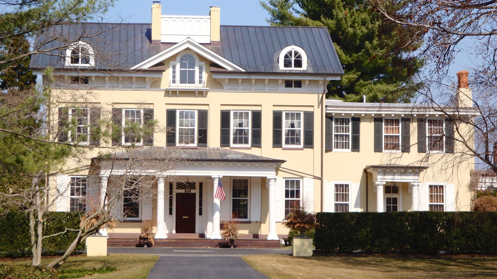 The front facade of a home, yellow with a grey roof. Photo by Zeete, CC BY SA