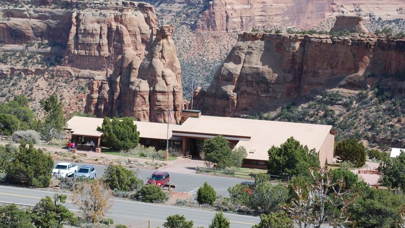 low, flat brown building surrounded by trees and parking lot, backdrop of steep canyon walls