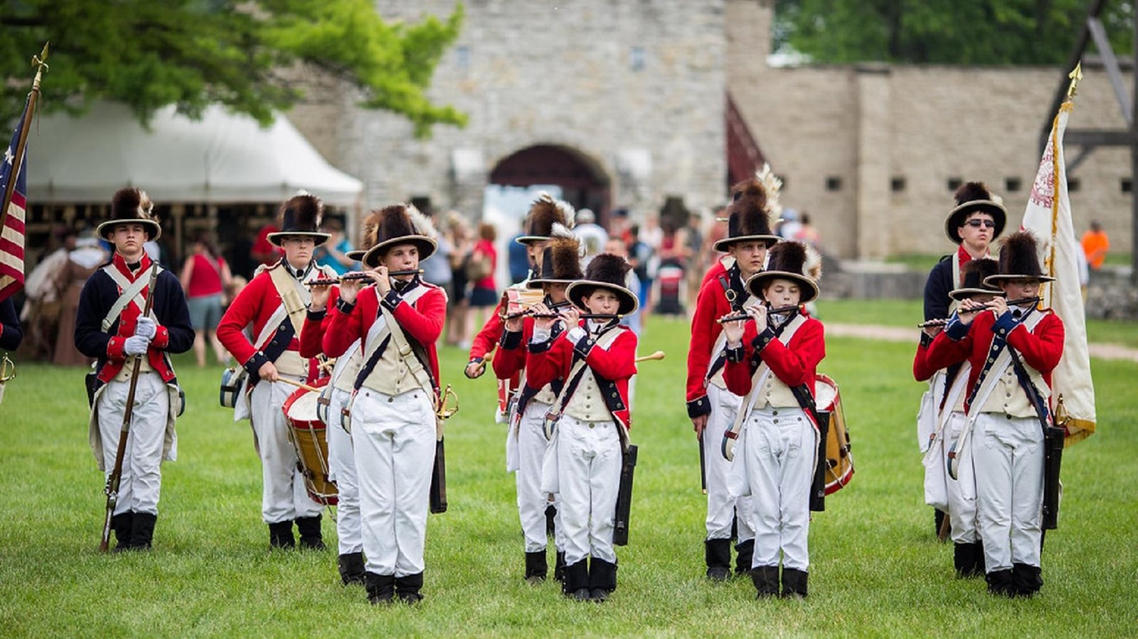 Young boys in 18th century costumes with flutes and drums stand in formation as a military band