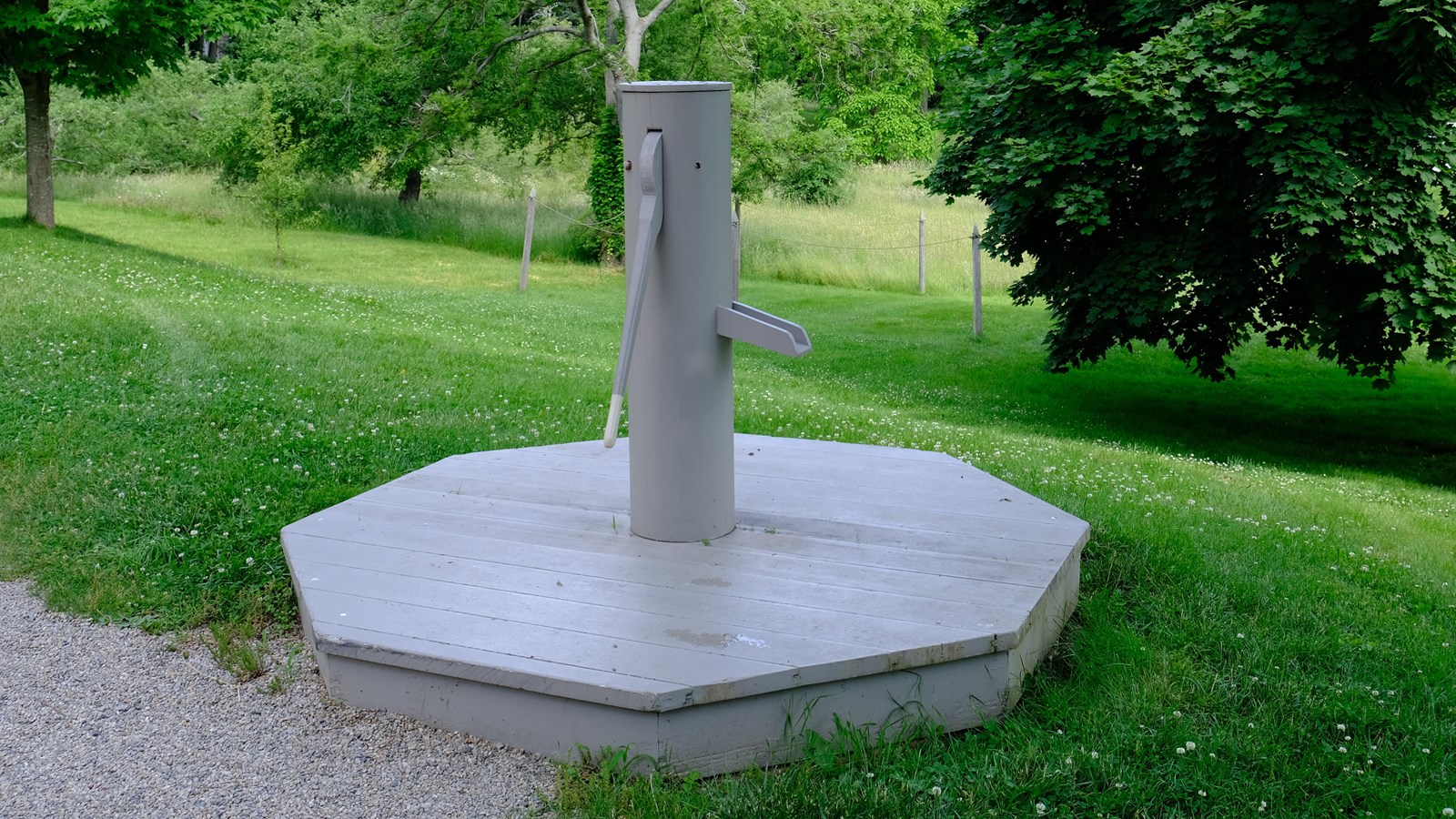 A grey wooden and metal water pump with handle and spout