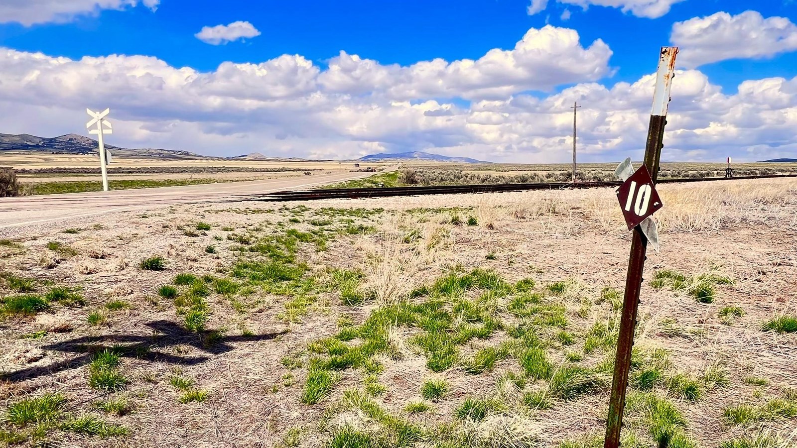 Marker #10 at the railroad crossing surrounded by green, yellow grassland