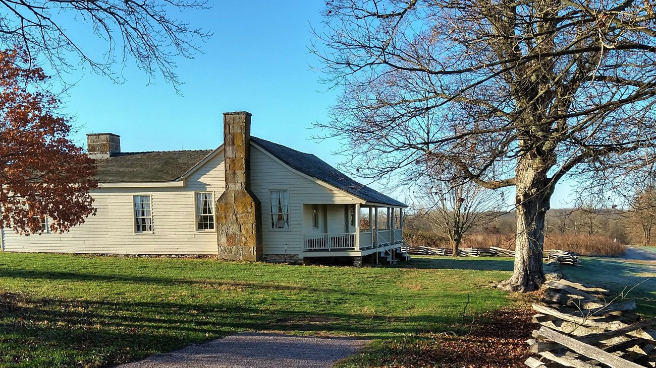 A historic farmhouse is bordered by trees and a wooden split-rail fence