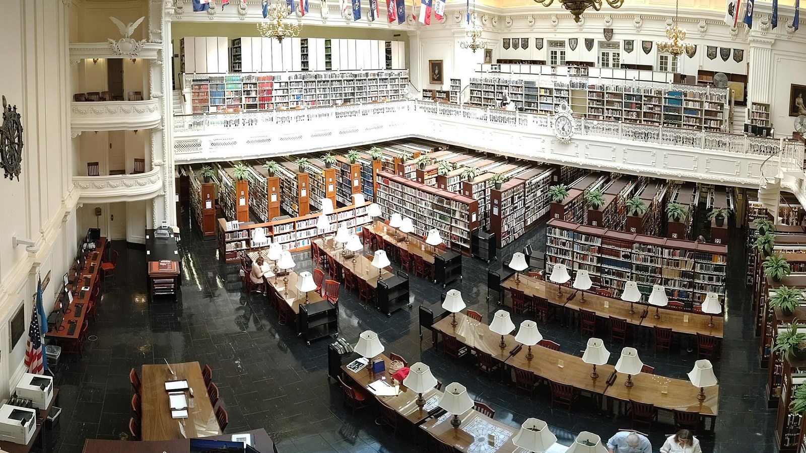 Shelves and desks in a large library room viewed from a balcony.