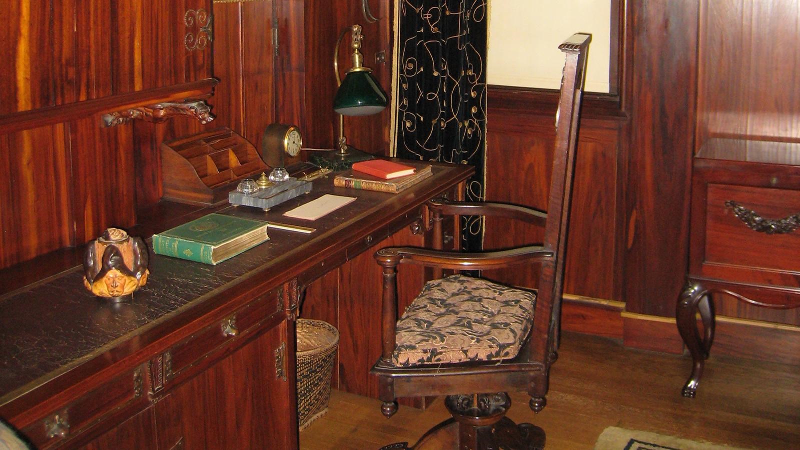 An small wood paneled office with built in desk and blue velvet window curtain.