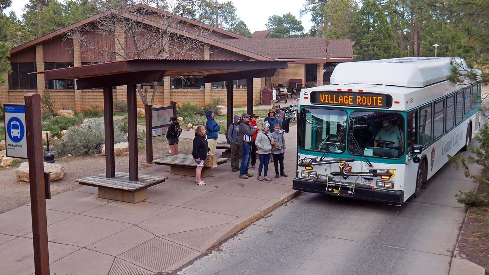 from under the roof of an open air bus shelter, several people are about to board a white and green 