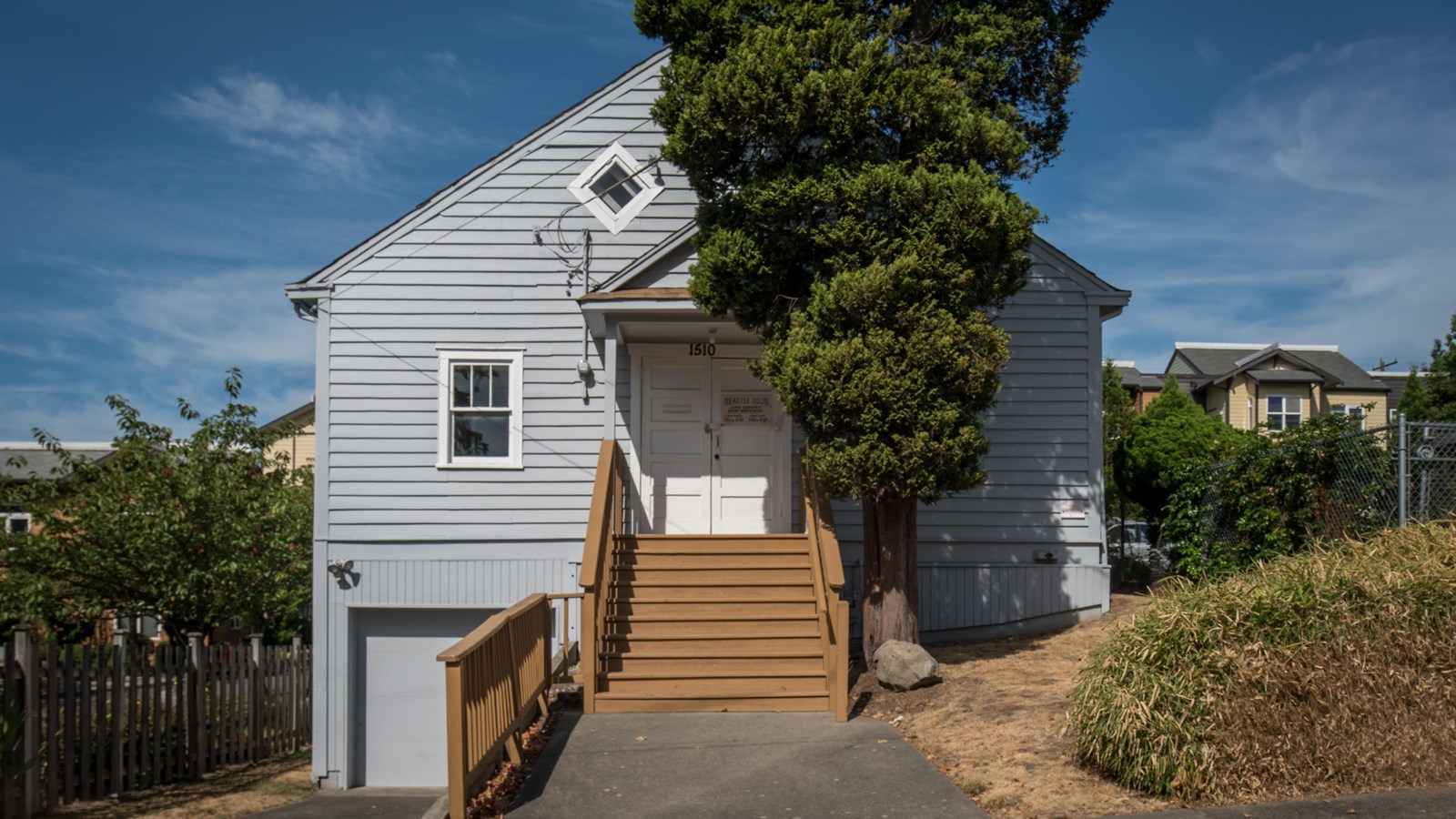 The building, fronted by a set of steps, stands out with its light grey clapboard exterior. 
